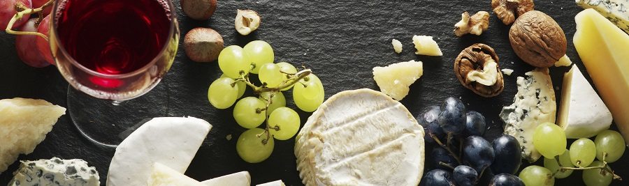 Different types of cheeses with wine glass and fruits. Top view.